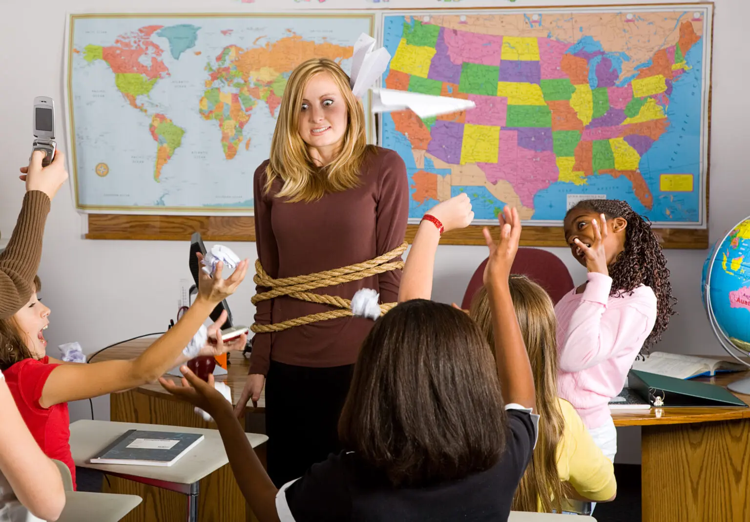 A teacher who is tied up in the middle of an unruly classroom of children